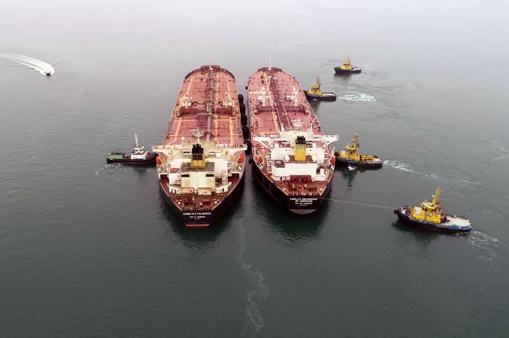 Vista aérea de dois navios petroleiros lado a lado em operação Ship to Ship, acompanhados por rebocadores